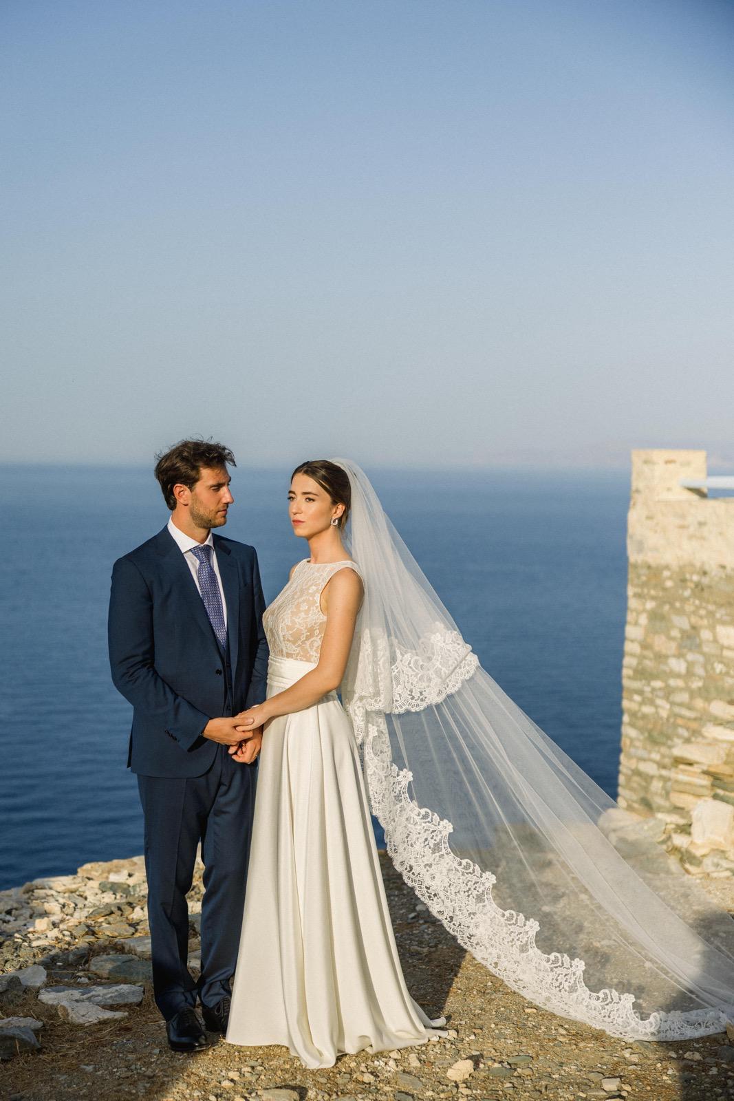A couple on the day of their wedding in front of the sea, the bride is wearing a long veil