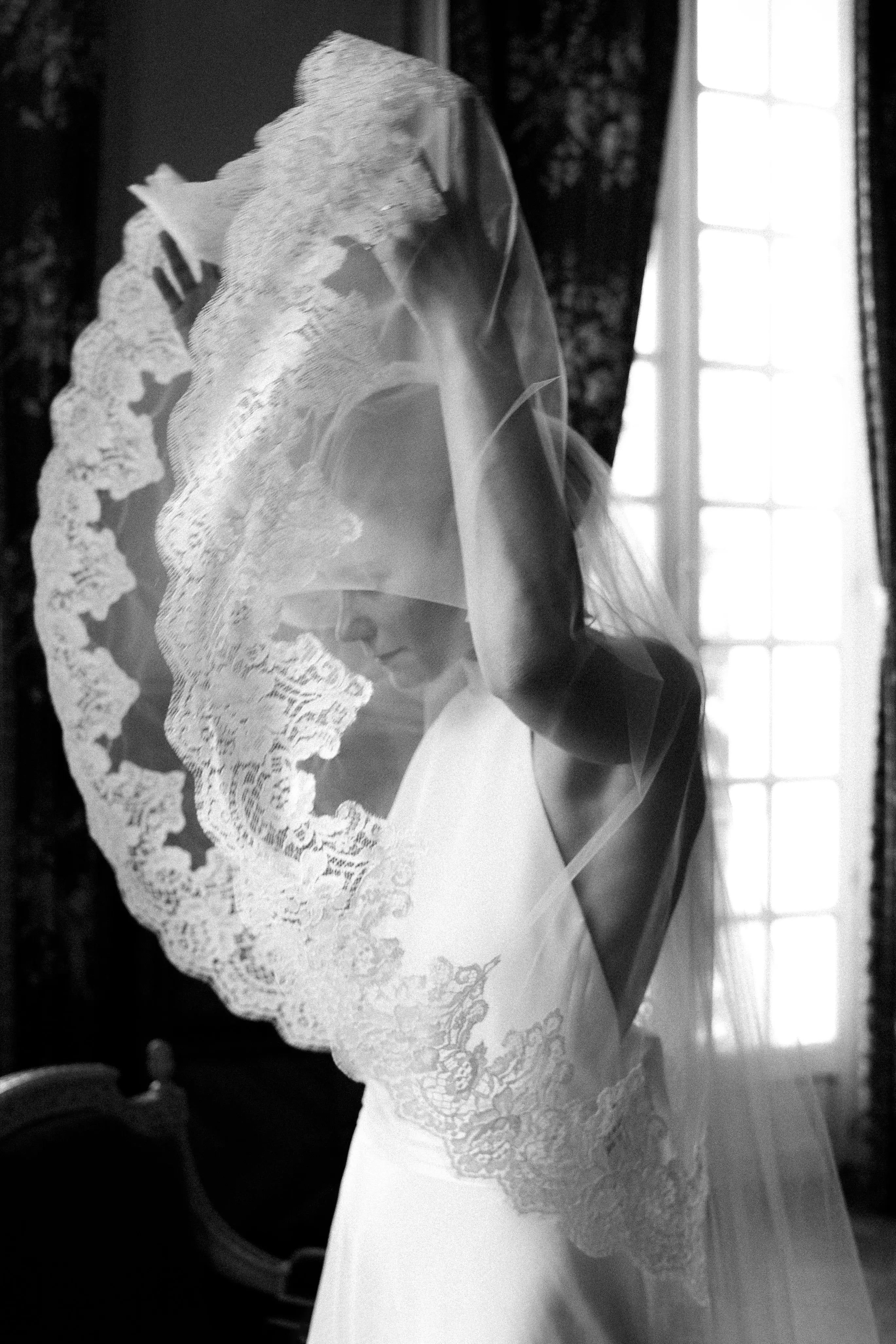 Bride lifting her wedding veil from their face and over her head. She is wearing an halterneck wedding dress.