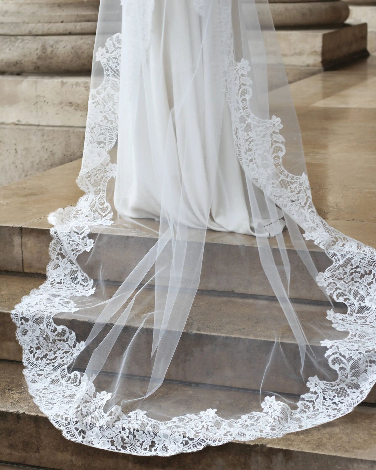 Floral Calais lace border of the Avec Toi veil spread over a marble staircase