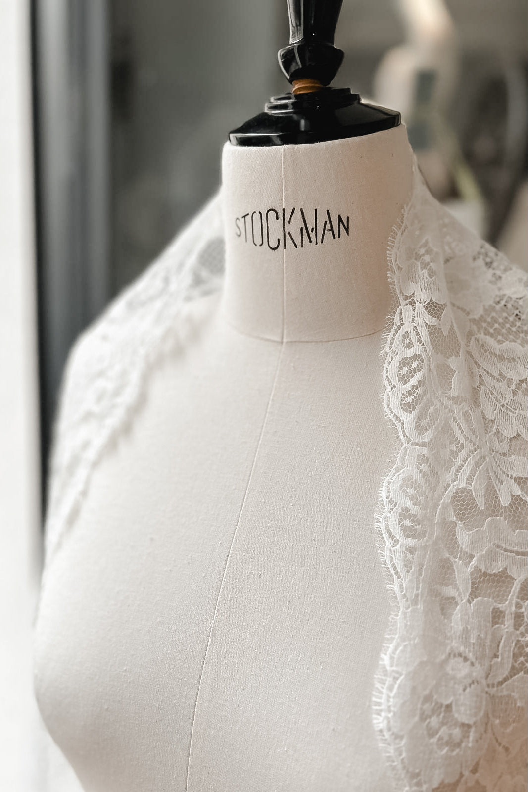 Lace mantilla resting on the shoulders of a dress form beside a window