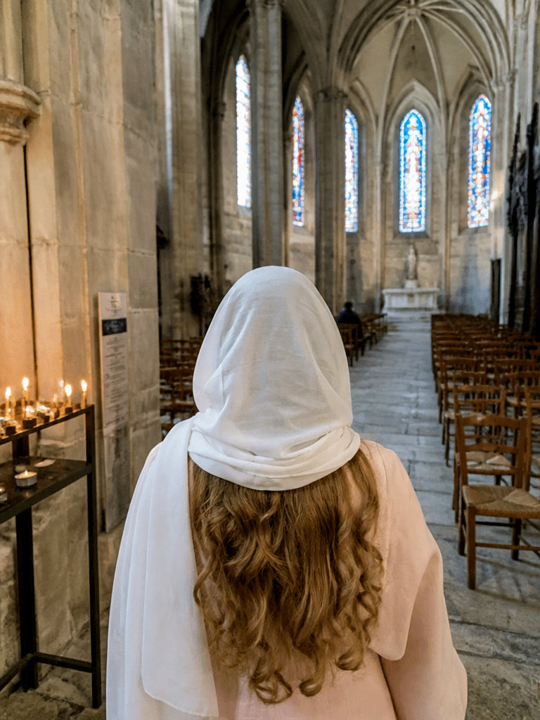 Ivory silk Christian prayer veil falling over the shoulders, seen from behind beside wooden church pews
