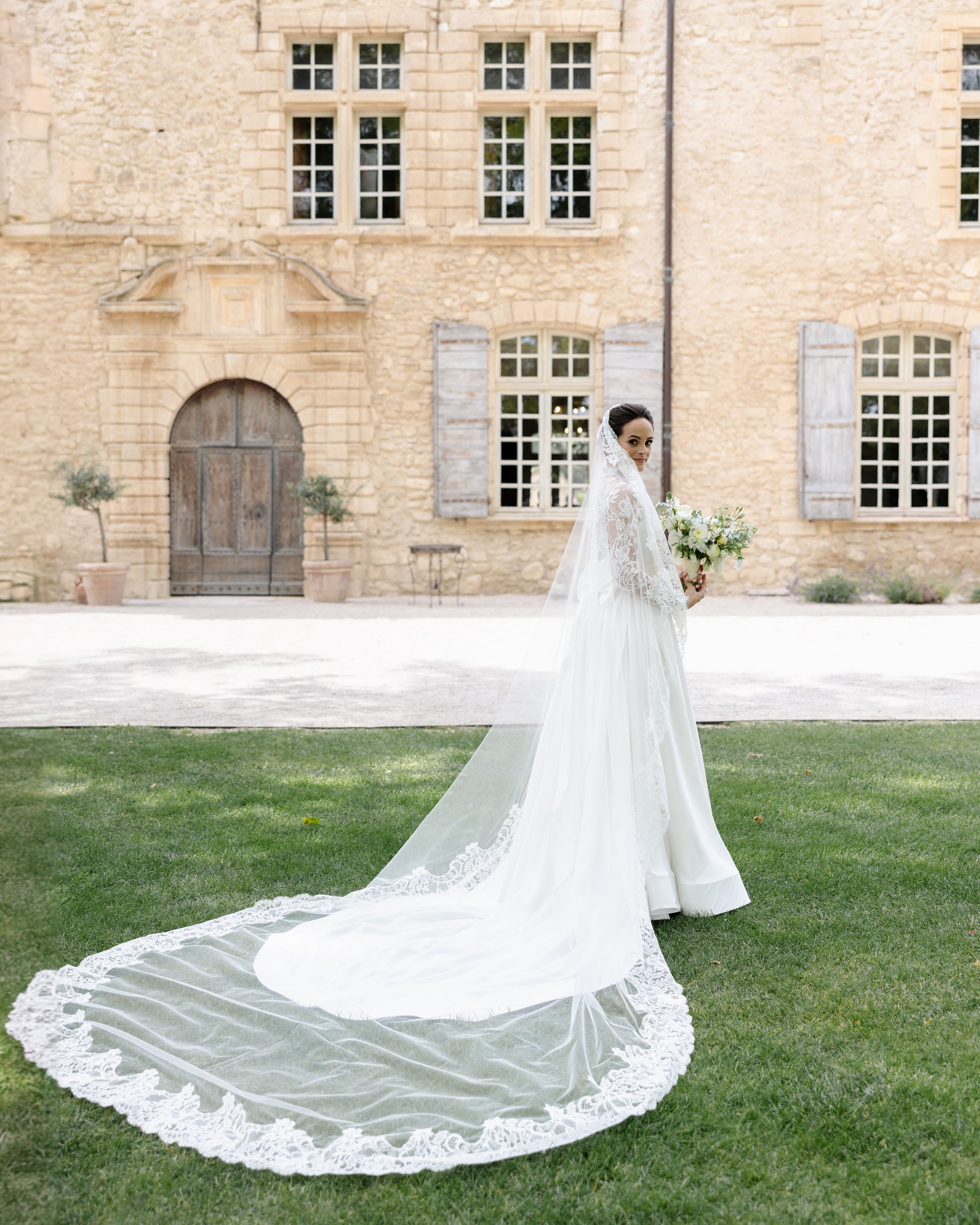 Bride standing in a garden wearing a lace mantilla wedding veil in her hair.