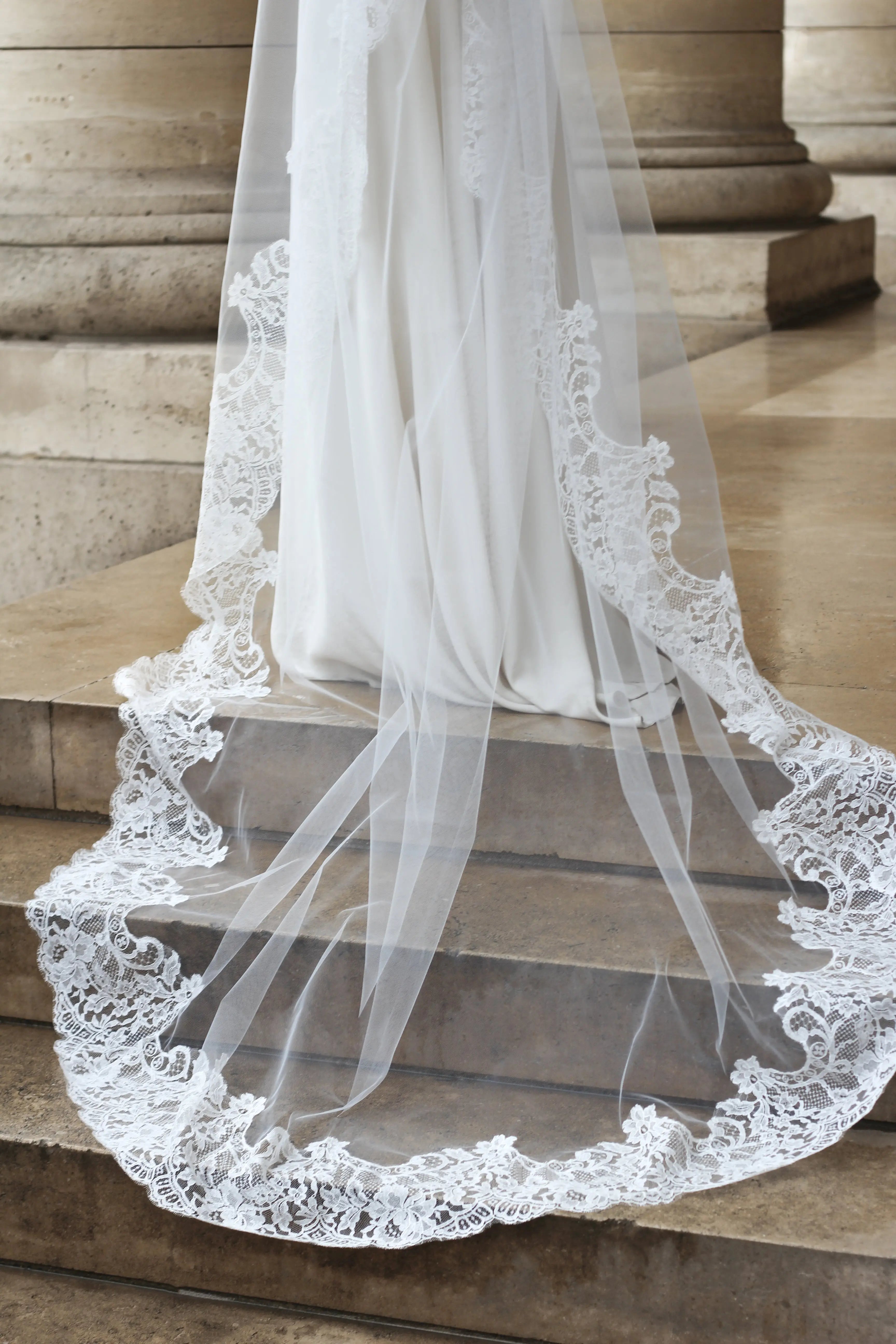 Floral details on the edge of a Calais lace wedding veil on a marbled staircase.