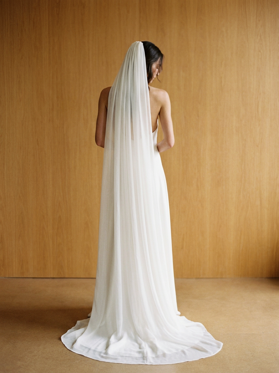 Full-length back view of a bride in a chapel-length silk chiffon veil pooling on the floor with a rounded edge, natural white silk