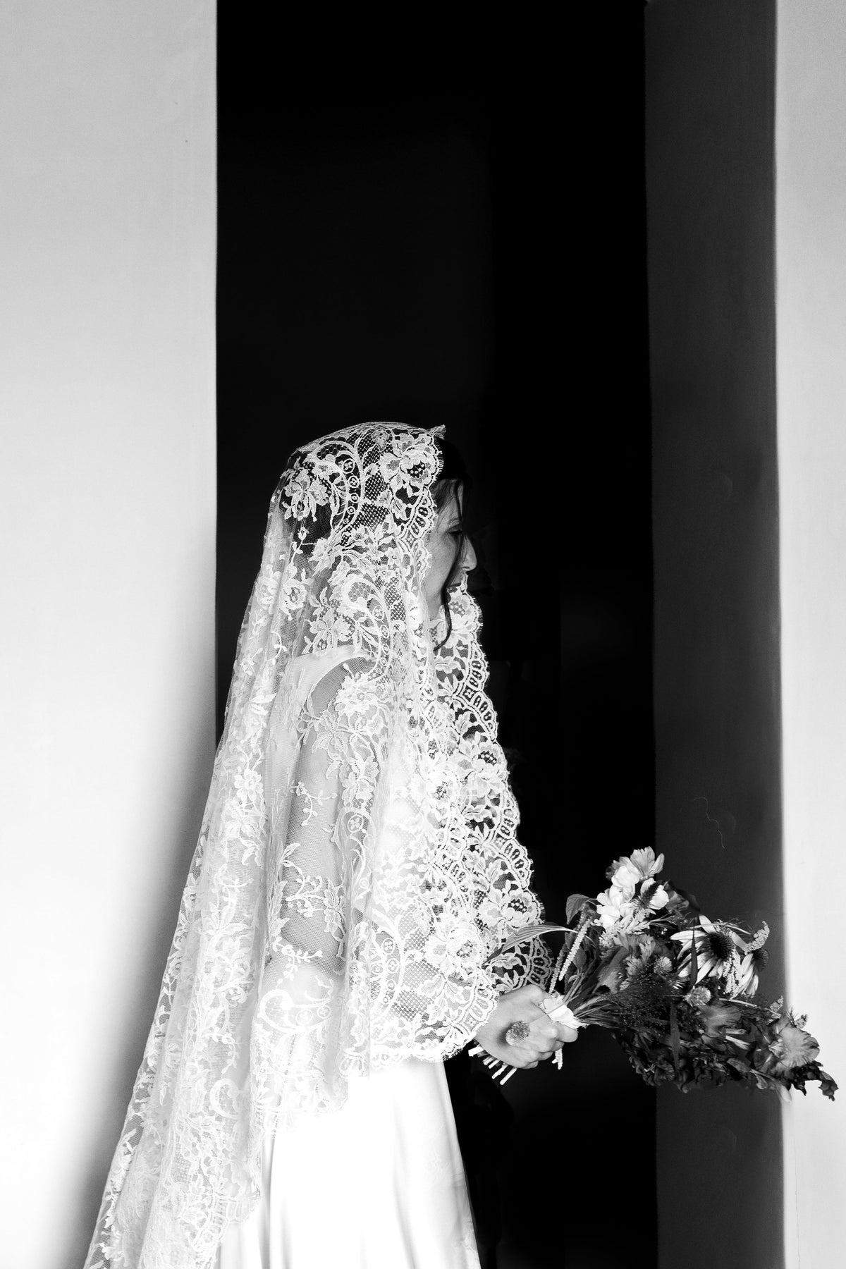 Black and white profile of a bride in Calais lace holding a loose bouquet