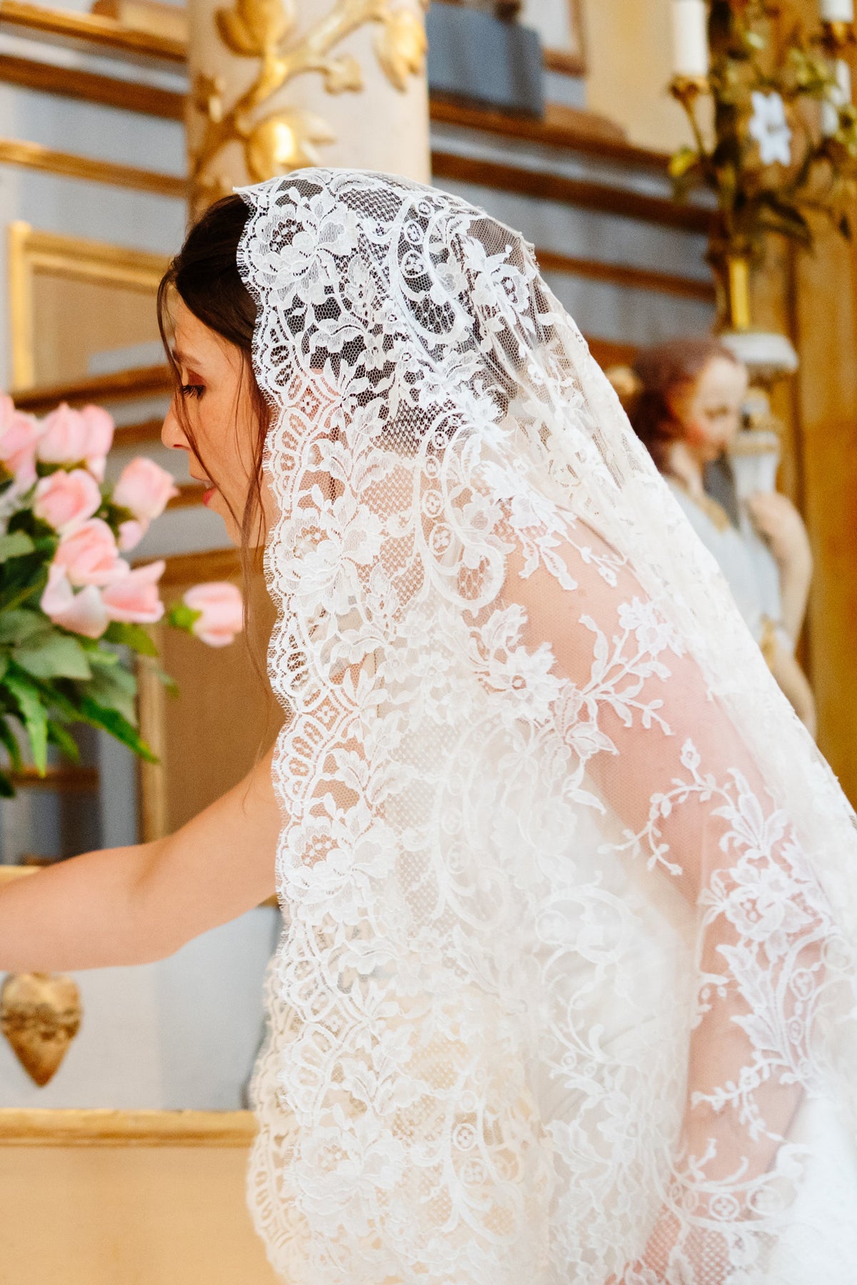 Bride in a full lace mantilla laying her bouquet at a gilded church altar