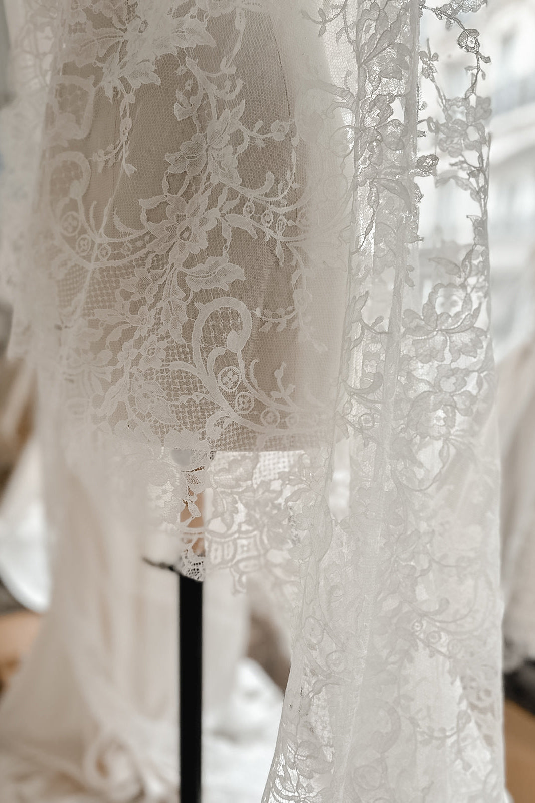Length of French lace spread over a wooden floor, showing the pattern of the train