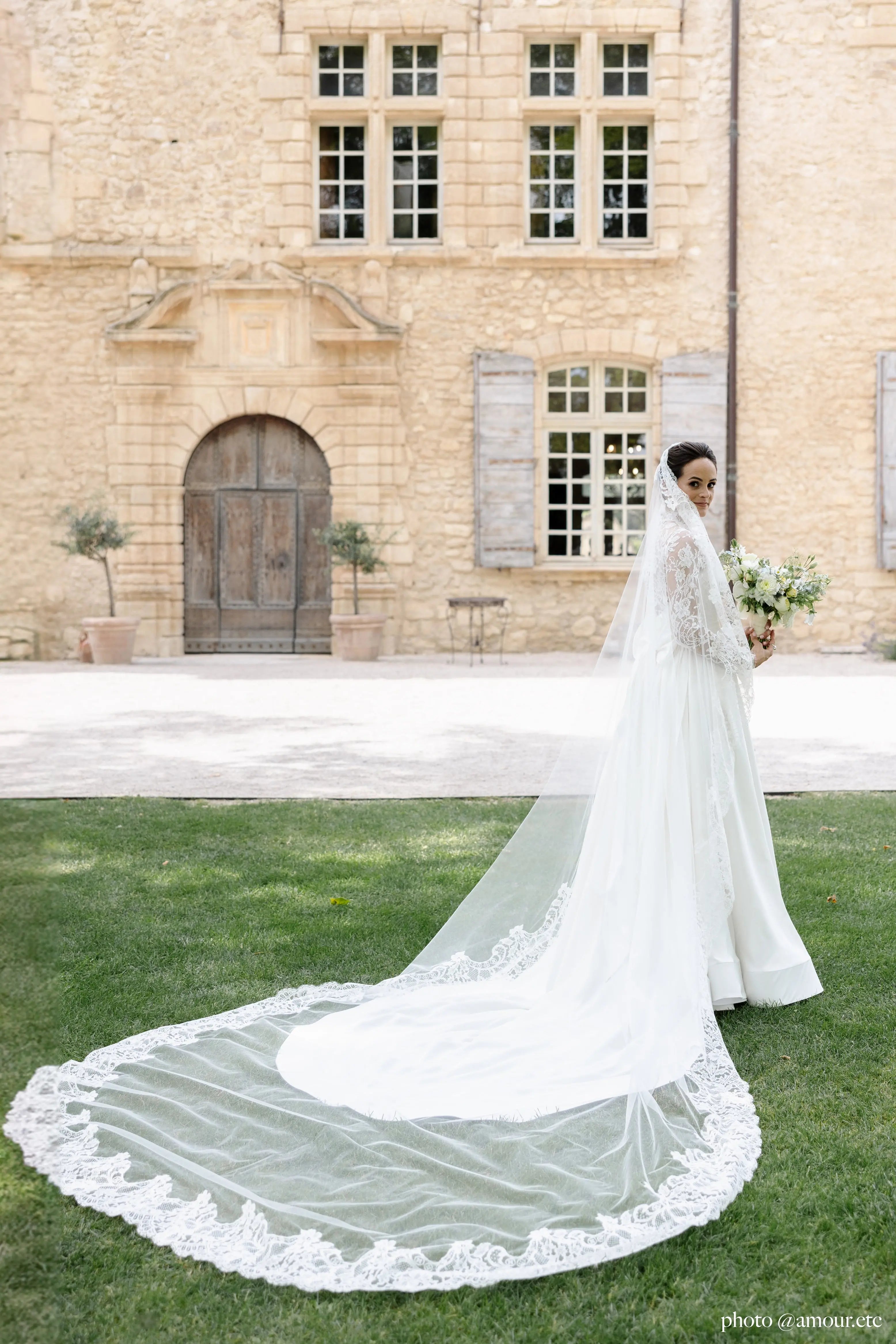 Bride standing in a garden wearing a lace mantilla wedding veil.