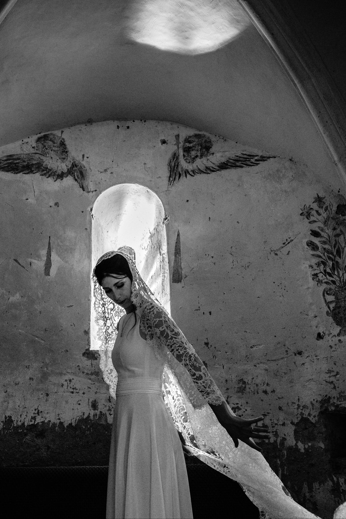 Black and white photo of a bride in a full lace mantilla beneath an arched chapel window
