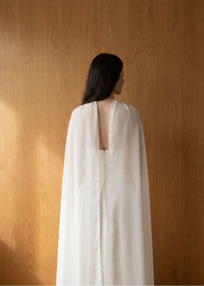 Back view of a sheer silk chiffon bridal cape over a fitted corseted wedding gown, natural white silk