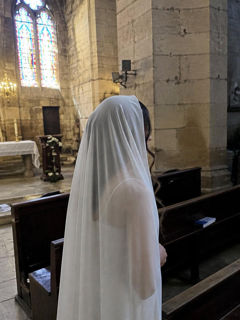 Woman in profile wearing the ivory silk georgette Traditional Christian Veil draped over her head in a Gothic church