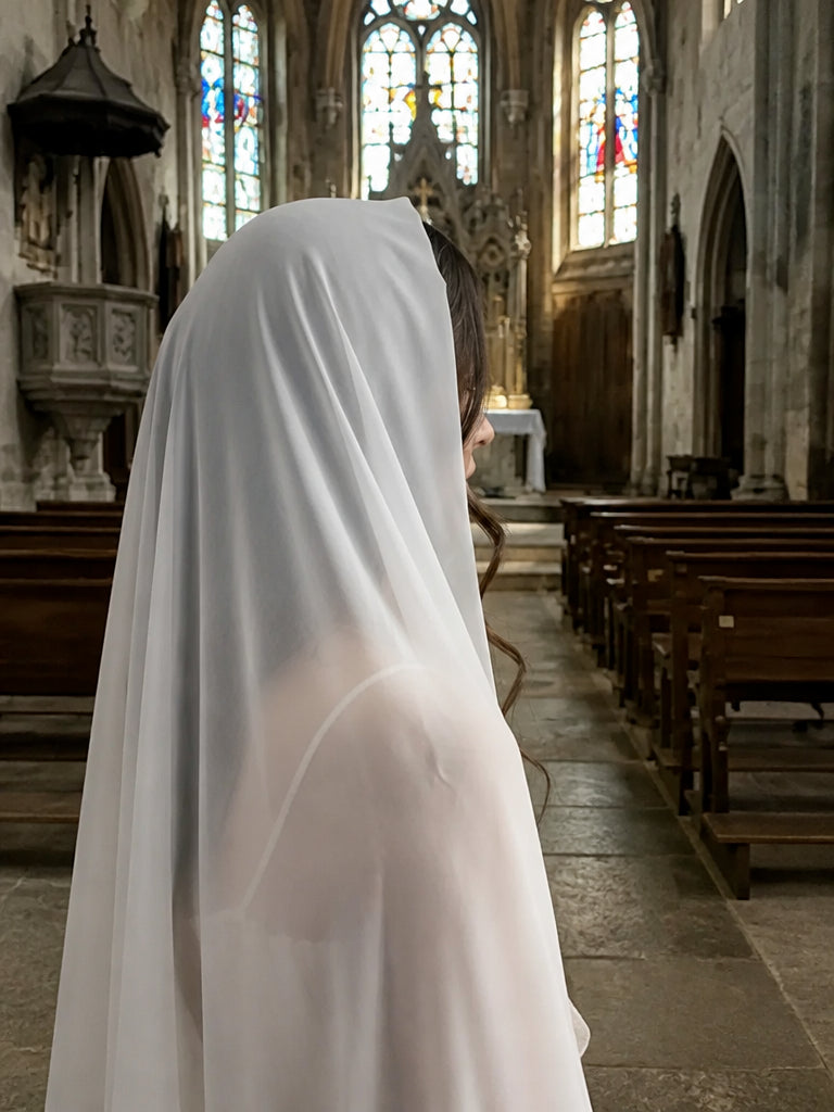 Woman with long red curls wearing the silk Christian veil wrapped around her head, next to prayer candles in a church