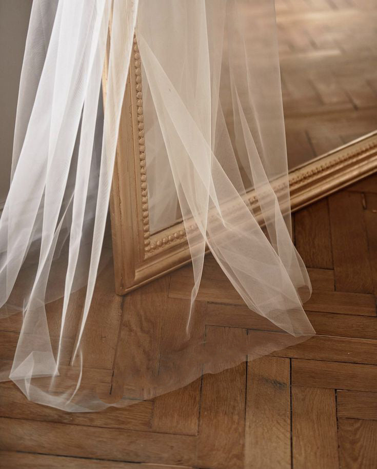 Voile de mariée long en tulle blanc transparent, délicatement posé contre un miroir dans un cadre élégant.